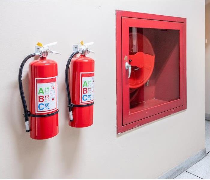 Two red fire extinguishers hanging on a white commercial workplace wall